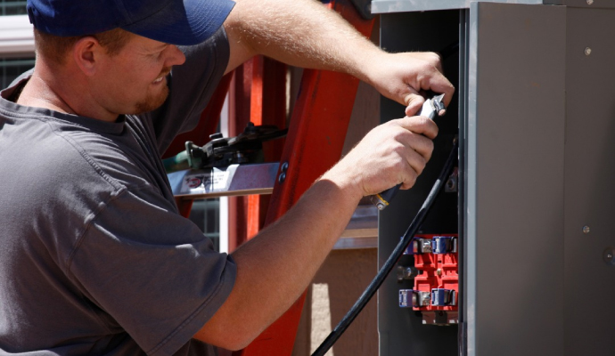 Person working on an electrical panel with red and black wires.